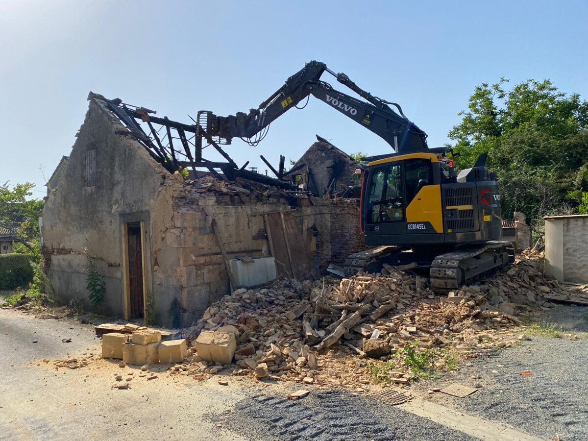 Vue du début de la démolition d'une habitation en ruine à l'aide d'une pelle mécanique.